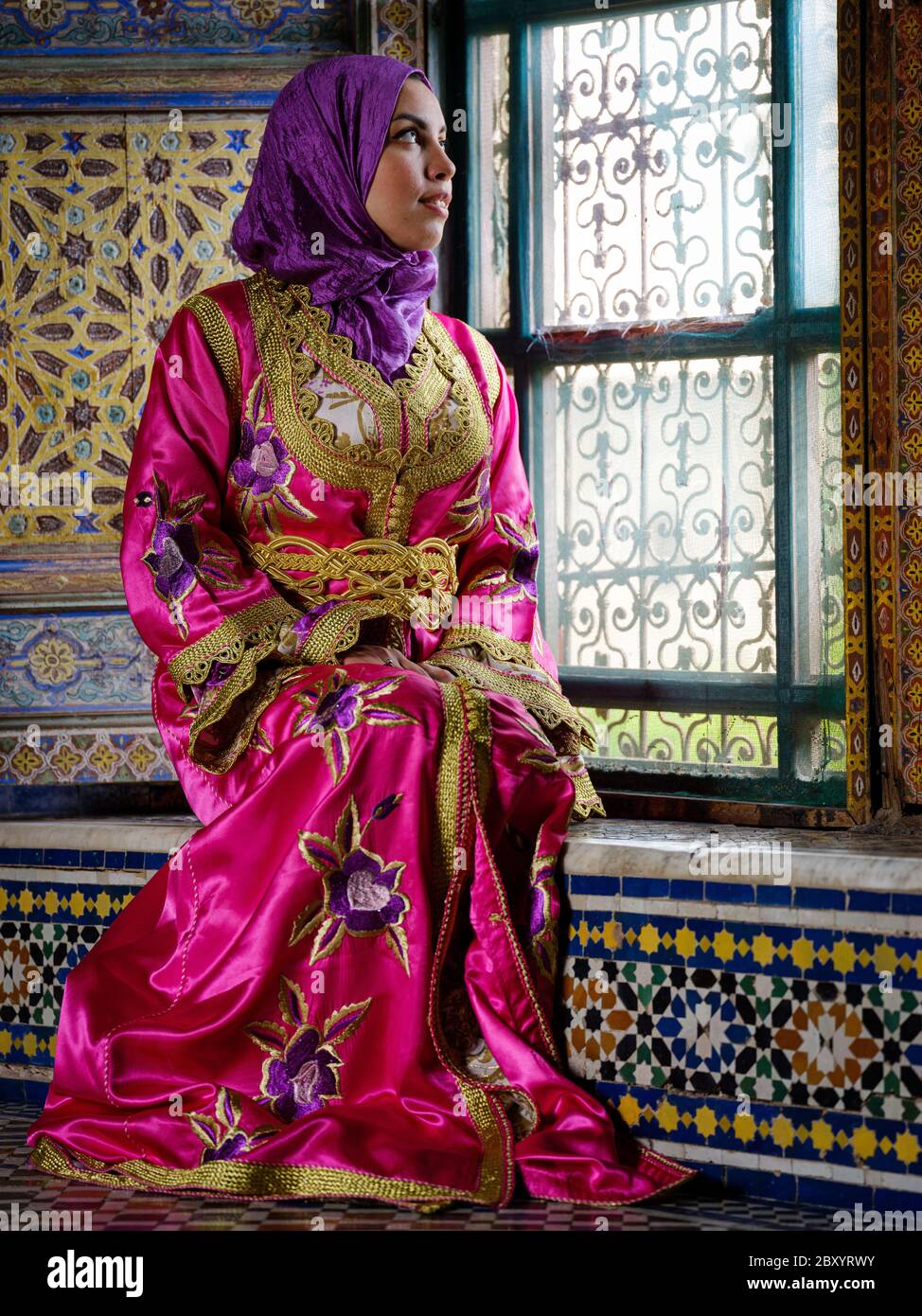 FÈS, MAROC - VERS MAI 2018 : jeune femme marocaine en robe traditionnelle assise par une fenêtre à Fès Banque D'Images