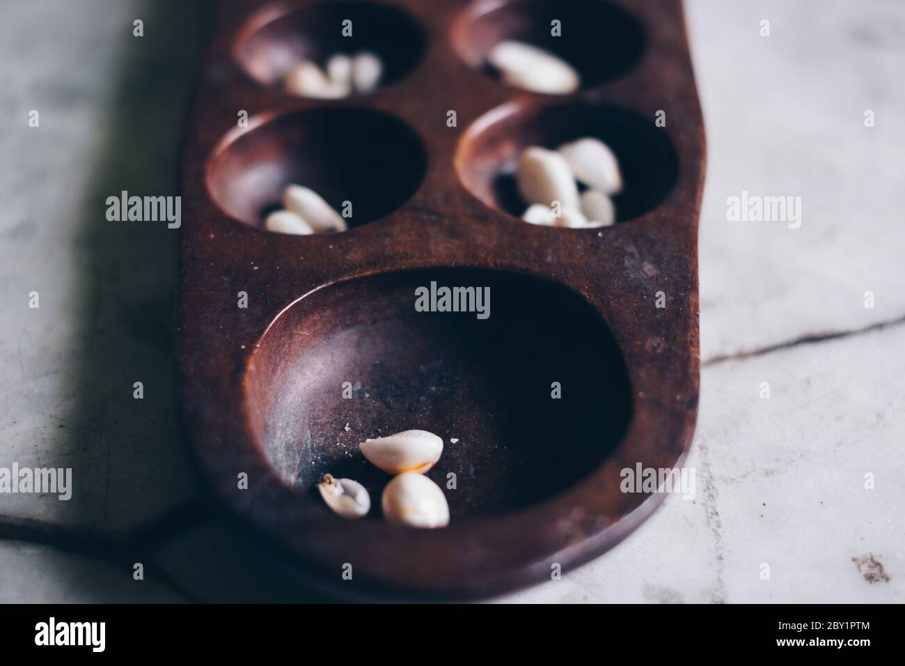 Gros plan de la partie tête de Sungka, jeu philippin mancala, sur une table en marbre blanc cassé avec des pièces de coquillages. Mise au point sélective. Banque D'Images