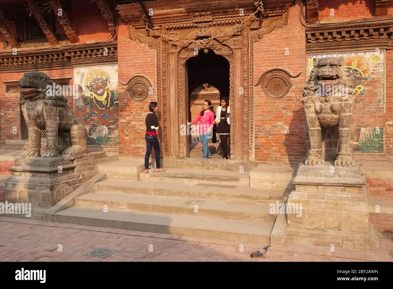 Trois jeunes femmes qui quittent le complexe du Palais Royal à Durbar Square, Patan, Katmandou Valley, Népal, la porte flanquée de deux lions de pierre Banque D'Images