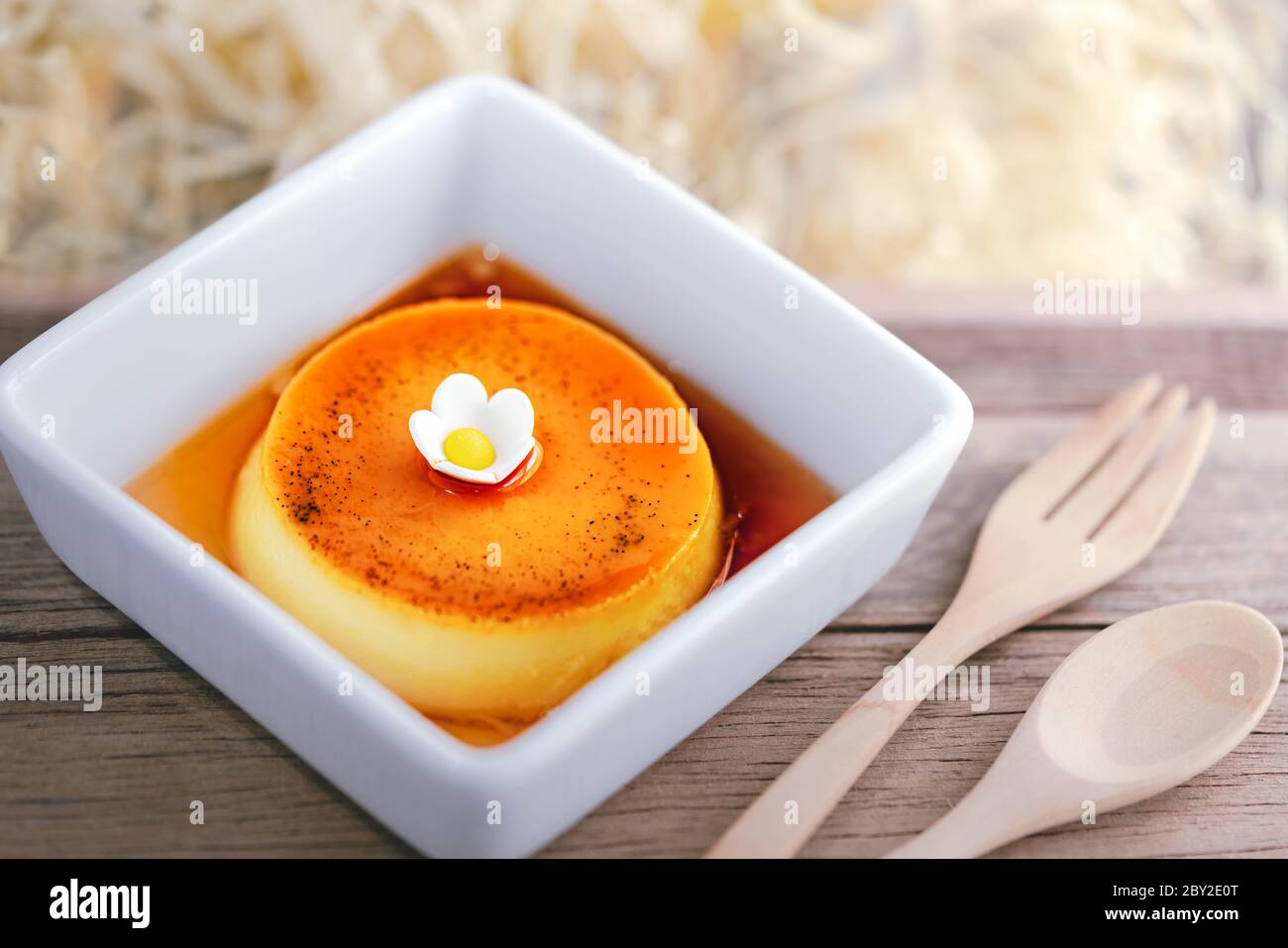 Pudding à la crème anglaise au caramel maison sur une assiette blanche avec fond de bois Banque D'Images