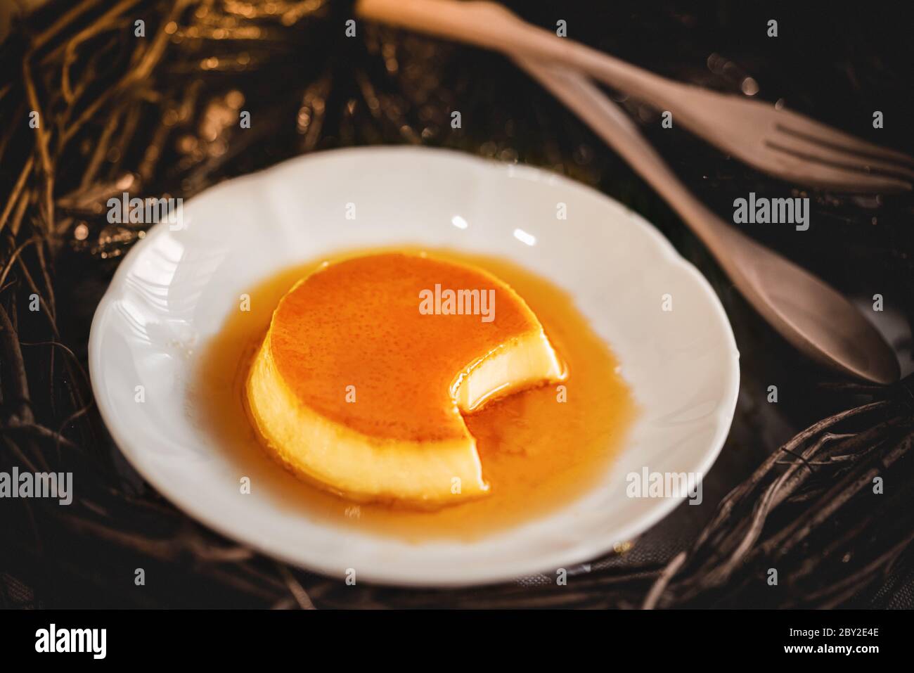 Pudding à la crème anglaise au caramel maison sur une assiette blanche avec fond de bois Banque D'Images