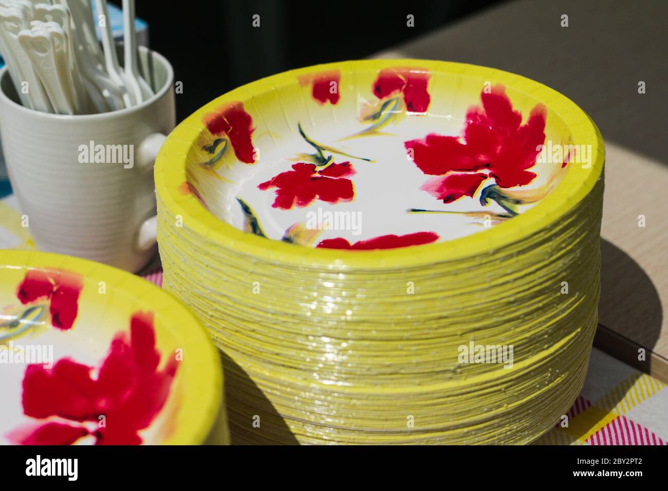 Assiette à motif fleuri empilée et tasse blanche sur la table. Assiette jaune colorée et motif de fleurs rouges. Banque D'Images