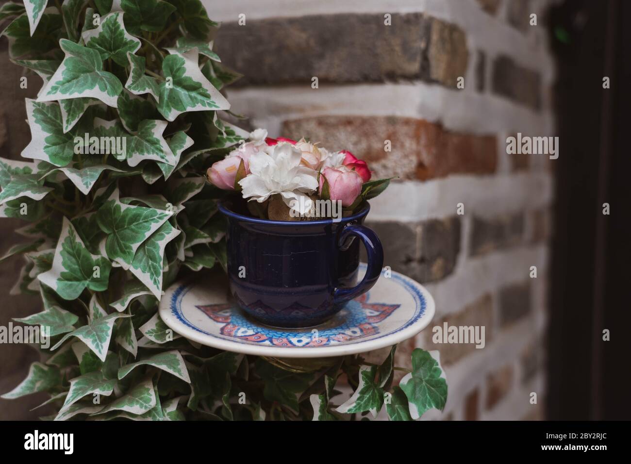 Tasse de thé bleue remplie de fleurs arrangement à l'intérieur avec la décoration de plante sur un mur de brique. Un ensemble de tasse de thé en céramique avec fleurs poussant à l'intérieur. Banque D'Images