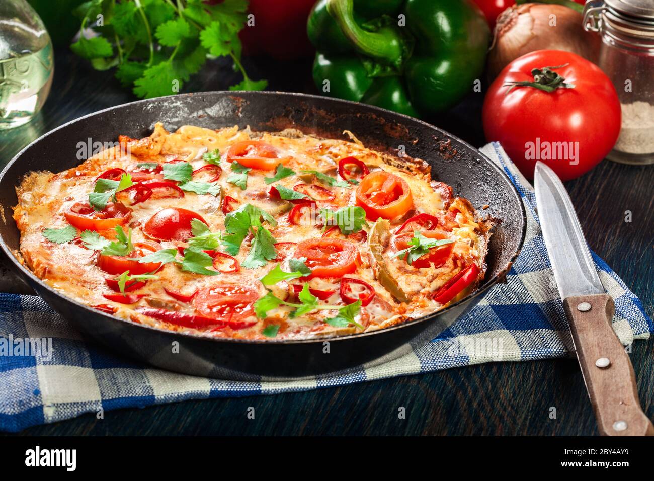 Frittata fait d'oeufs, saucisse chorizo, poivron rouge, poivron vert, tomates, fromage et piment dans une poêle sur table en bois. Cuisine italienne Banque D'Images