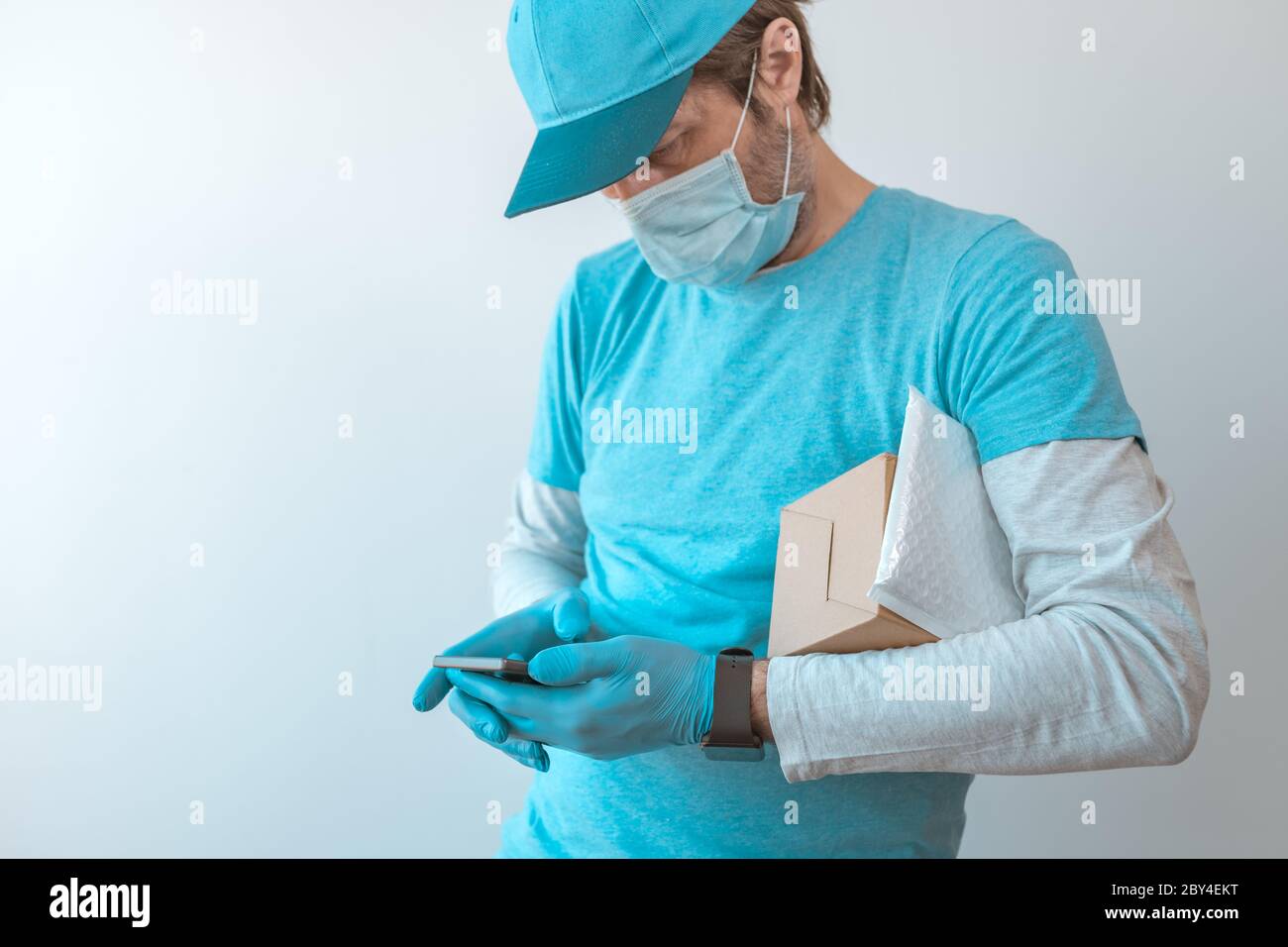 Homme de livraison avec des vêtements de protection utilisant un smartphone avec des gants de protection pendant une pandémie d'infection virale, foyer sélectif Banque D'Images