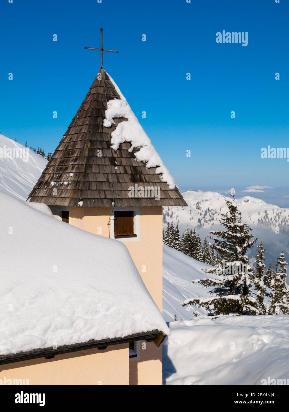 Vue détaillée de la tour de montagne de l'église avec croix sur le dessus dans le paysage alpin d'hiver enneigé le jour d'hiver ensoleillé. Alpes, Autriche, Europe. Banque D'Images