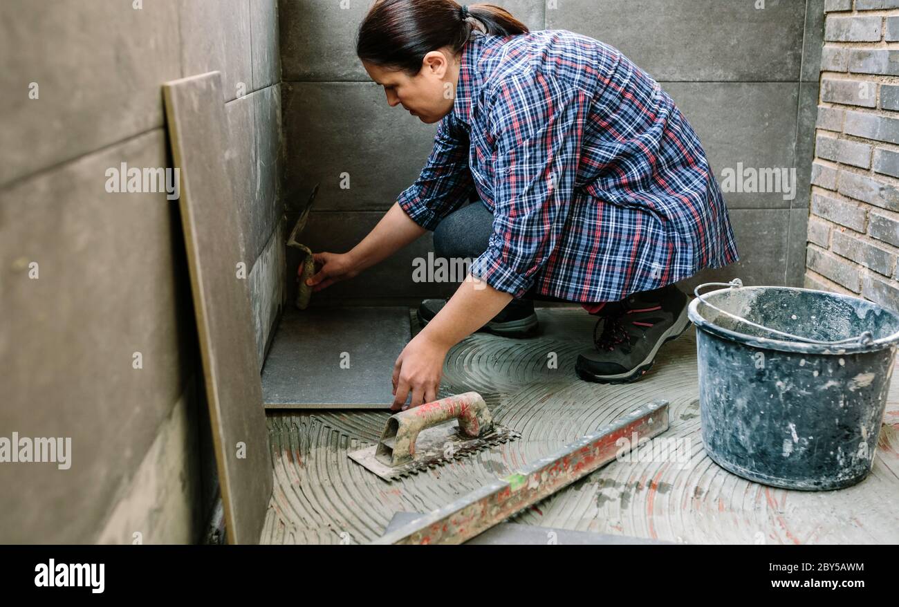 Femme ouvrier posant un nouveau plancher de carrelage Banque D'Images
