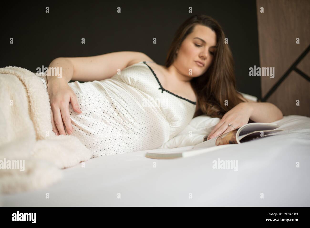 Belle femme enceinte lire un livre tout en étant allongé sur un lit à la maison Banque D'Images