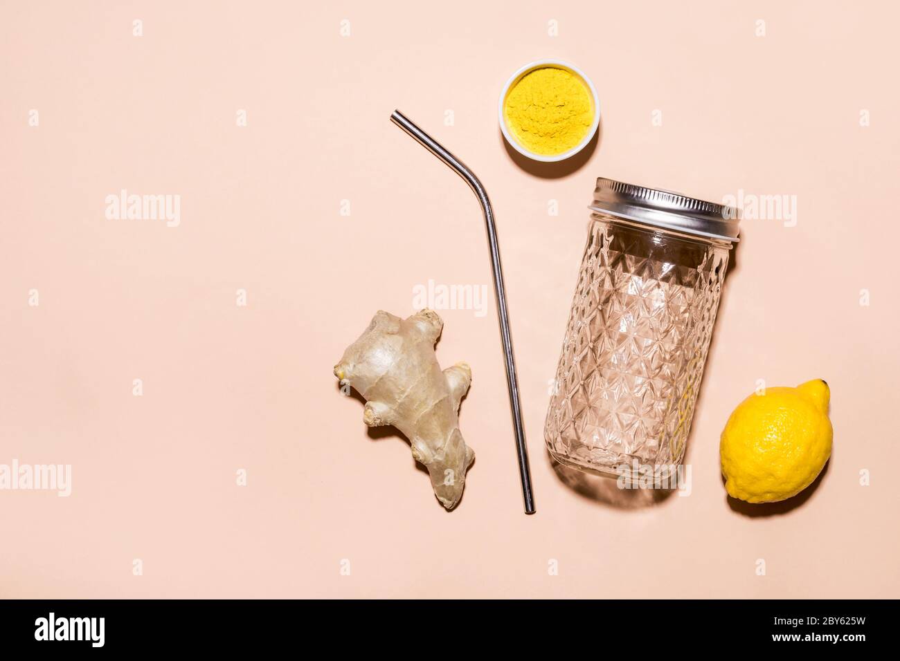 Ingrédients pour faire de l'eau de gingembre et un élégant bol avec une paille métallique sur fond beige. Banque D'Images