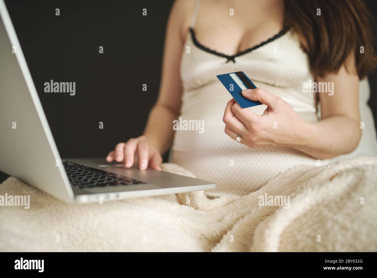 Une femme pensive magasiner en ligne avec une carte de crédit et un ordinateur portable, assis sur un canapé à la maison. Jeune femme enceinte surfer net, acheter des marchandises pour nouveau-né Banque D'Images