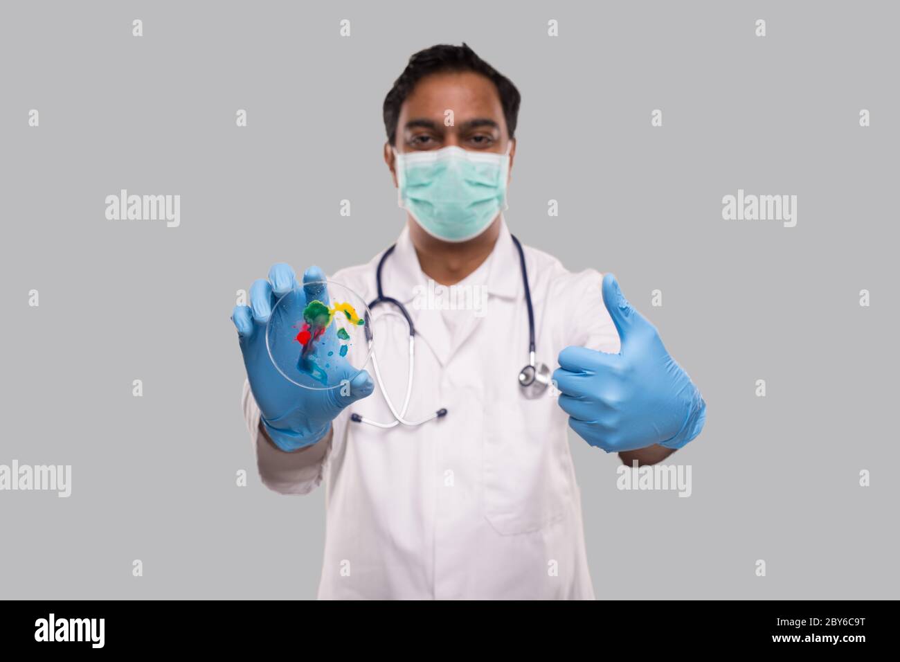 Médecin tenant une boîte de Petri portant un masque médical et des gants montrant le pouce vers le haut isolé. Médecine, concept de la science Banque D'Images