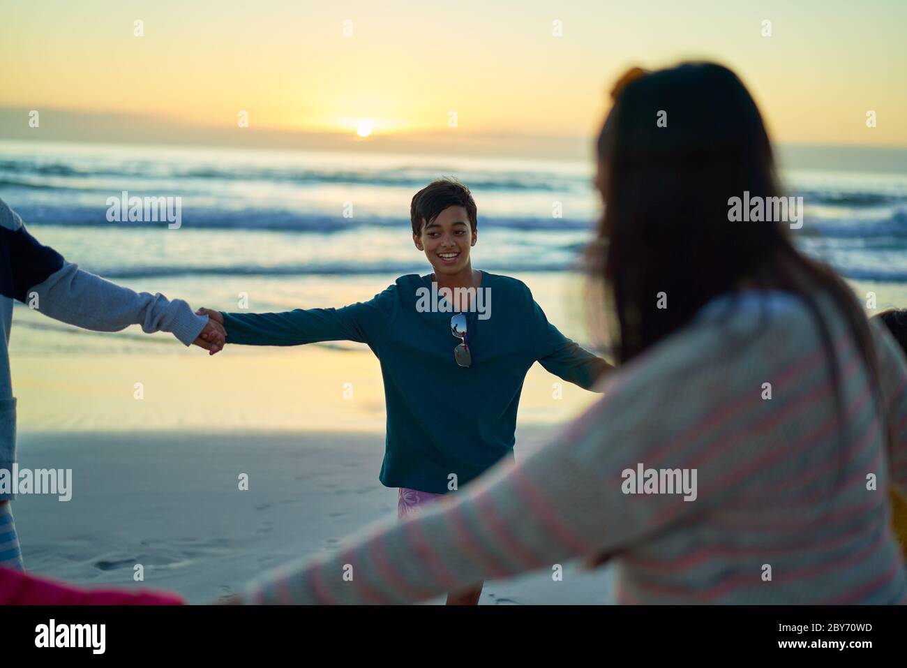 Bonne famille tenant les mains en cercle sur la plage de l'océan au coucher du soleil Banque D'Images