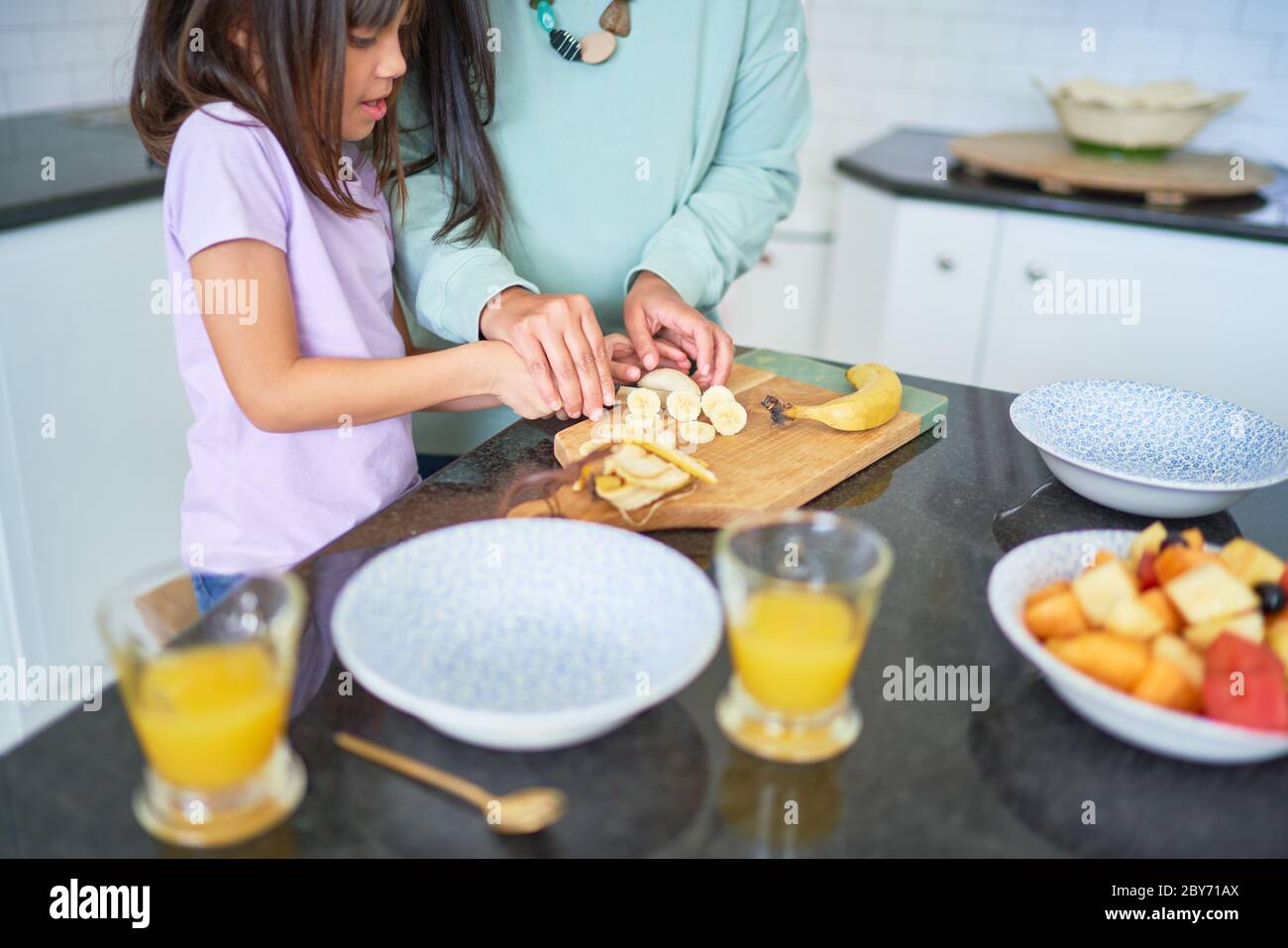 Mère et fille coupant des bananes dans la cuisine Banque D'Images