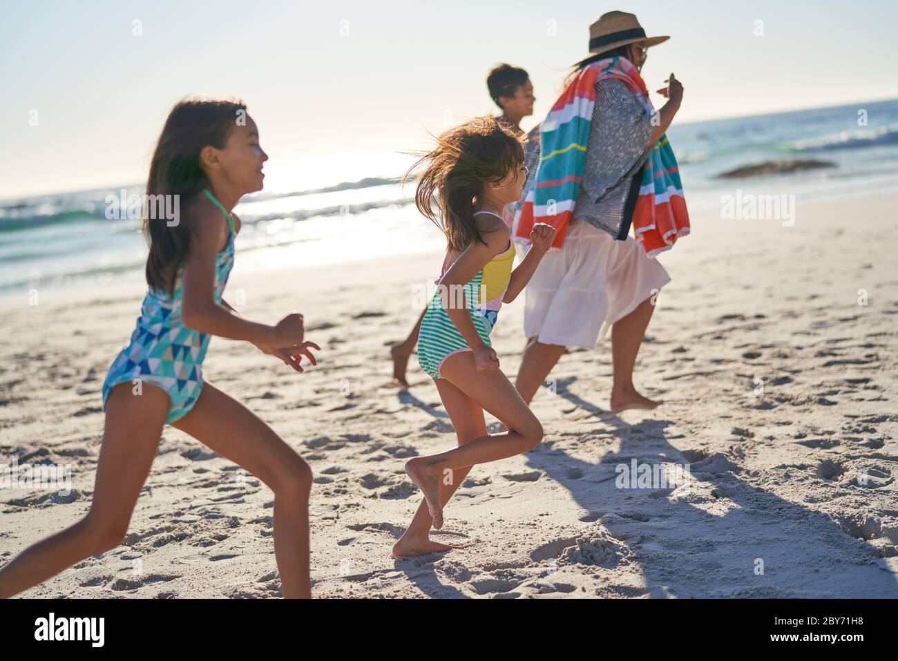 Famille ludique qui court sur une plage ensoleillée Banque D'Images