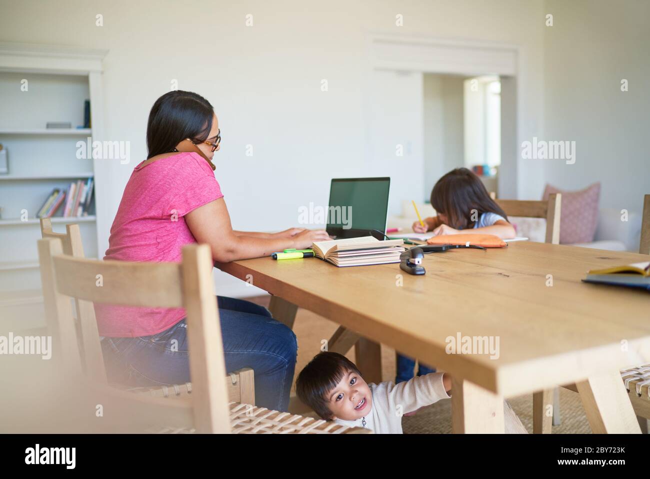 Mère travaillant sur un ordinateur portable avec des enfants jouant et faisant leurs devoirs Banque D'Images