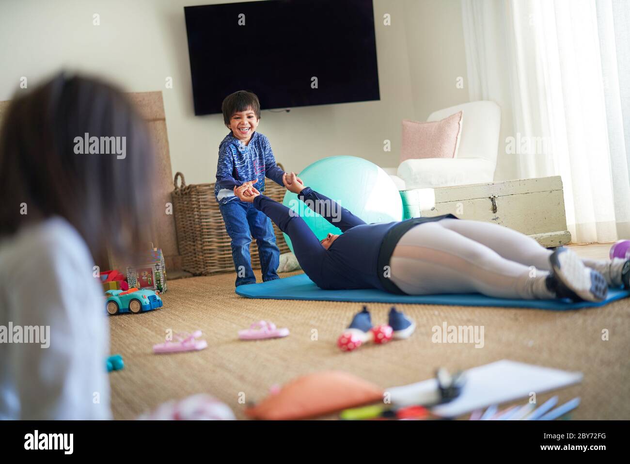 Garçon jouant avec la mère s'exerçant sur le tapis de yoga dans la salle de séjour Banque D'Images