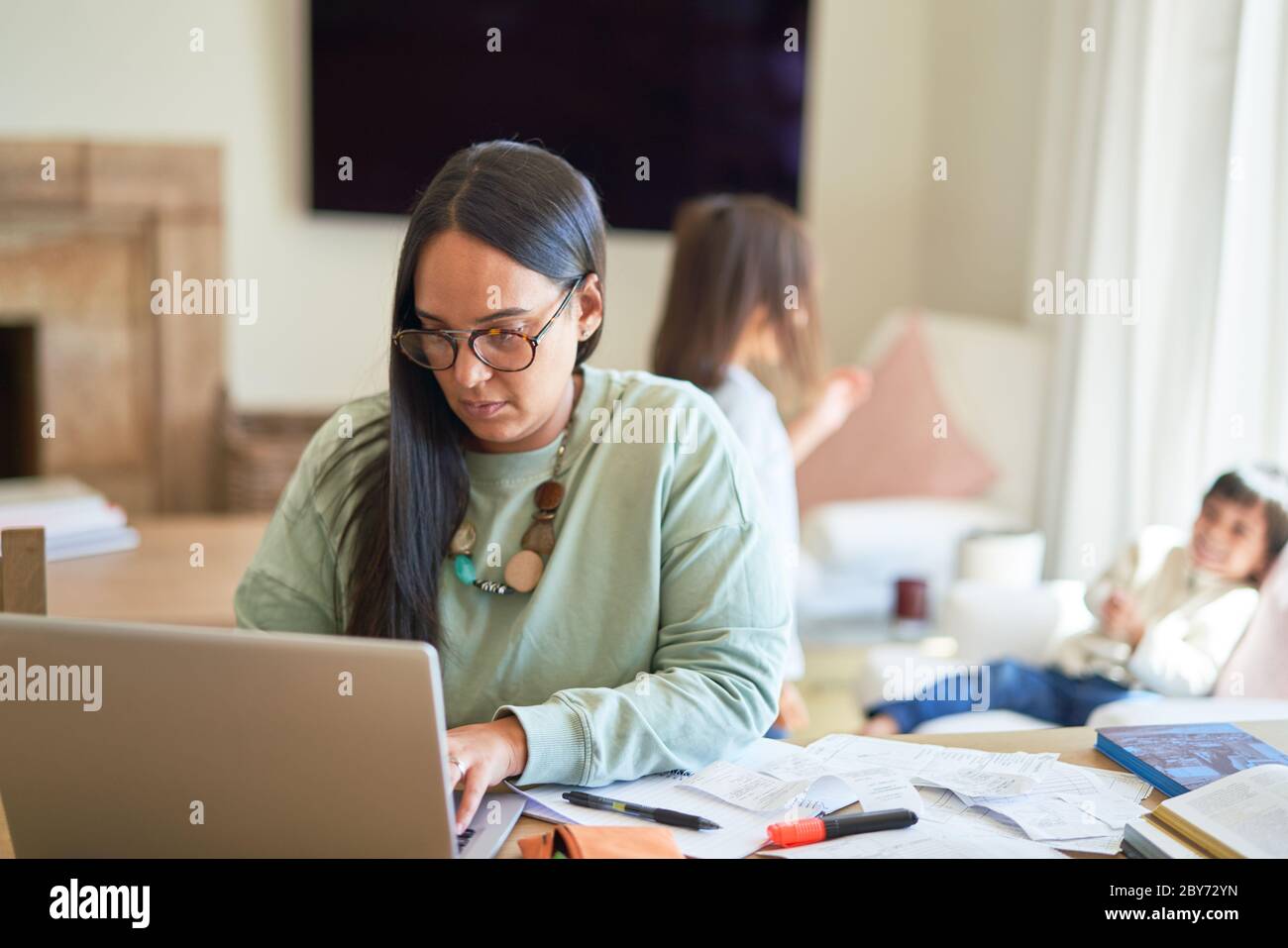 Mère payant des factures sur ordinateur portable avec des enfants en arrière-plan Banque D'Images