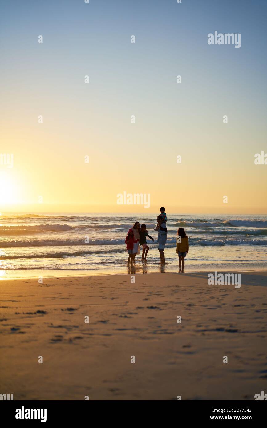 La famille se coupera dans l'océan sur la plage au coucher du soleil Banque D'Images