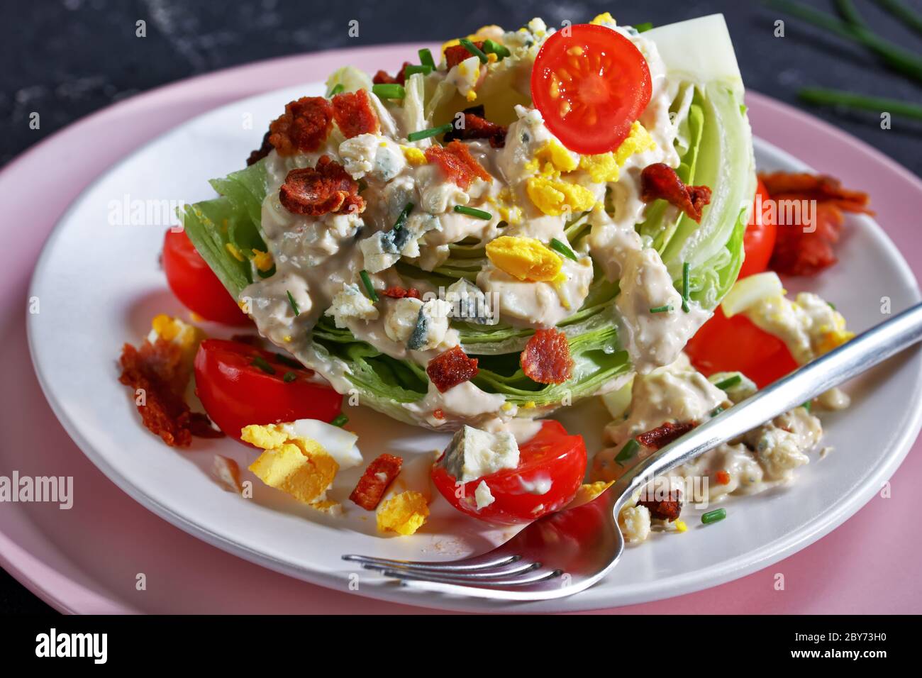 gros plan de la salade iceberg recouverte de sauce au fromage bleu, bacon croustillant, tomates cerises, œufs durs émiettés, ciboulette sur les assiettes Banque D'Images