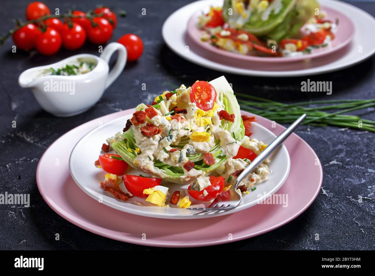 gros plan de la salade iceberg recouverte d'une vinaigrette au fromage bleu, bacon croustillant, tomates cerises, œufs durs, ciboulette sur des assiettes sur un béret Banque D'Images