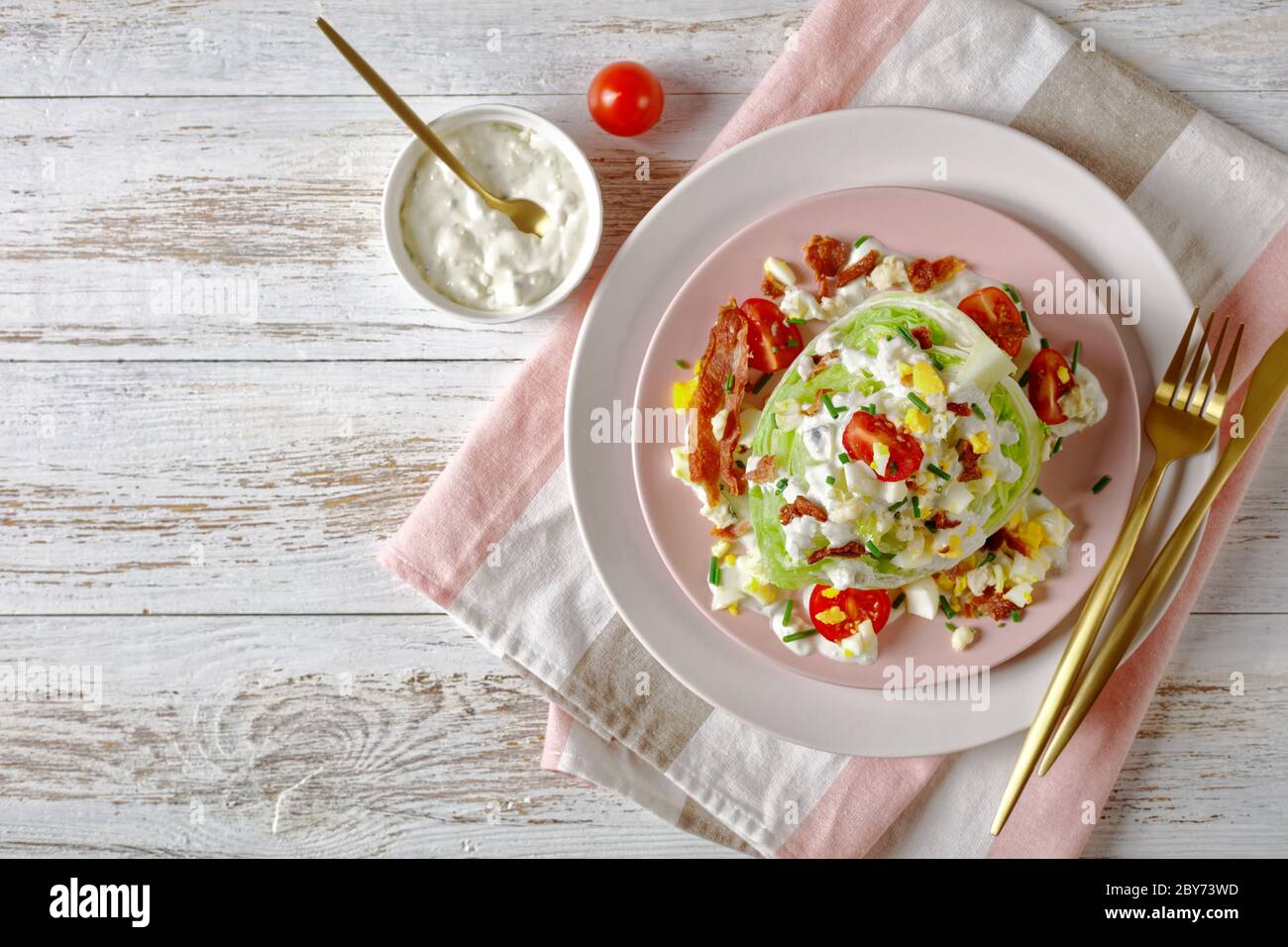 salade iceberg au fromage bleu, bacon croustillant, tomates cerises, œufs durs émiettés, ciboulette sur des assiettes roses sur un blanc Banque D'Images