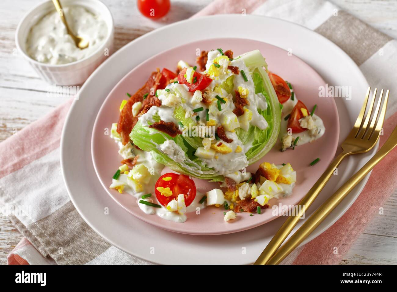 salade iceberg avec sauce au fromage bleu, bacon croustillant, tomates cerises, œufs durs émiettés, ciboulette sur des assiettes roses avec des morceaux dorés Banque D'Images