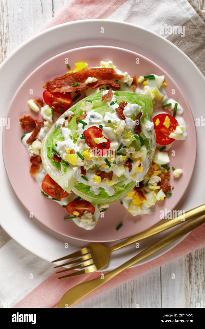salade iceberg avec sauce au fromage bleu, bacon croustillant, tomates cerises, œufs durs émiettés, ciboulette sur des assiettes roses avec des morceaux dorés Banque D'Images