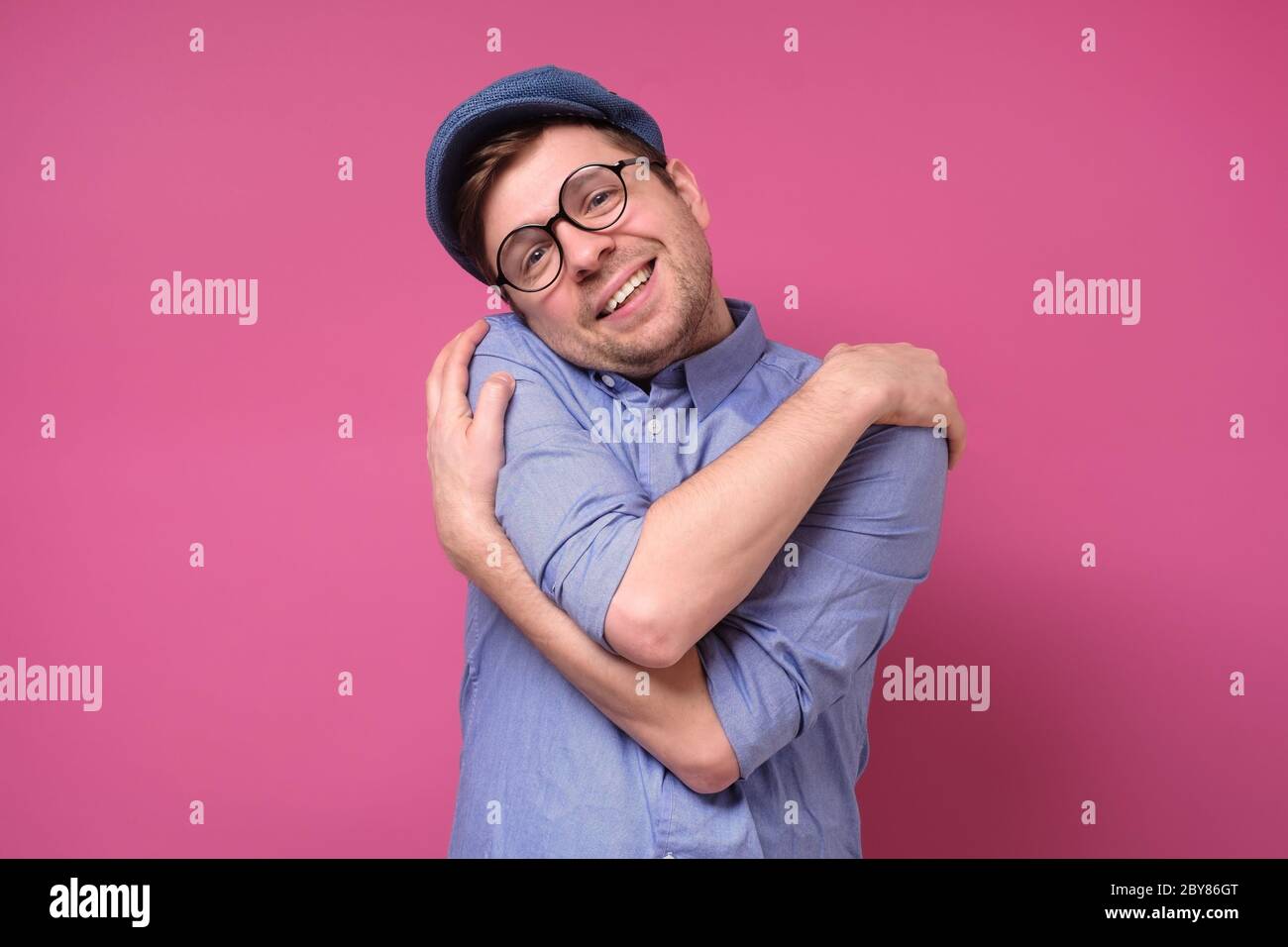 Heureux caucasiens homme se hous lui-même, a une grande estime de soi, a un sourire en dents de souris. Studio tourné sur un mur rose. Banque D'Images