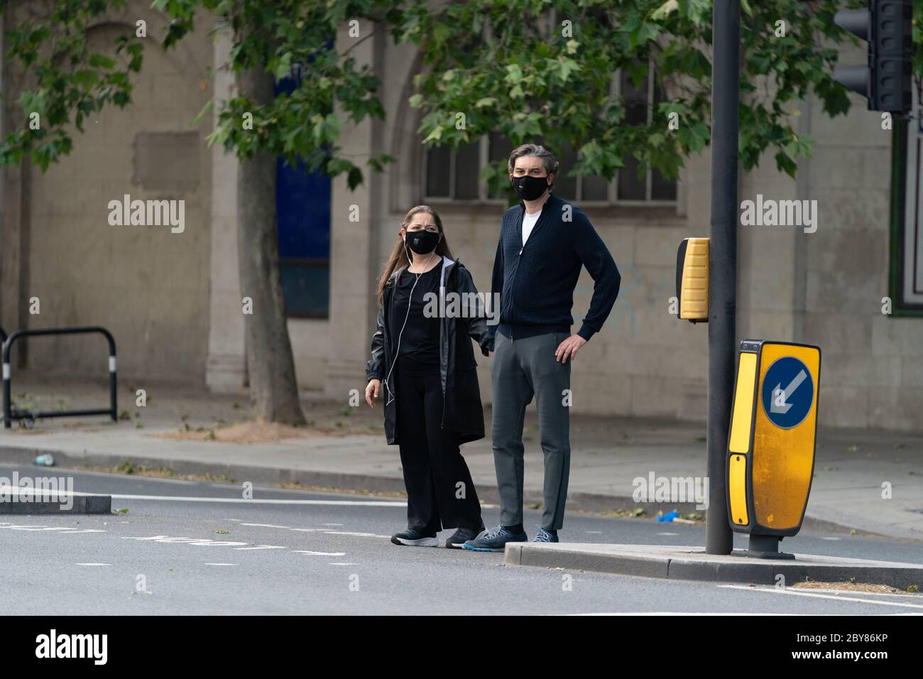 Couple marchant le long de l'Embankment à Londres, Angleterre portant des maks dans le serrucklocklockbox pandémique COVID-19 du coronavirus en traversant la route - 1 Banque D'Images