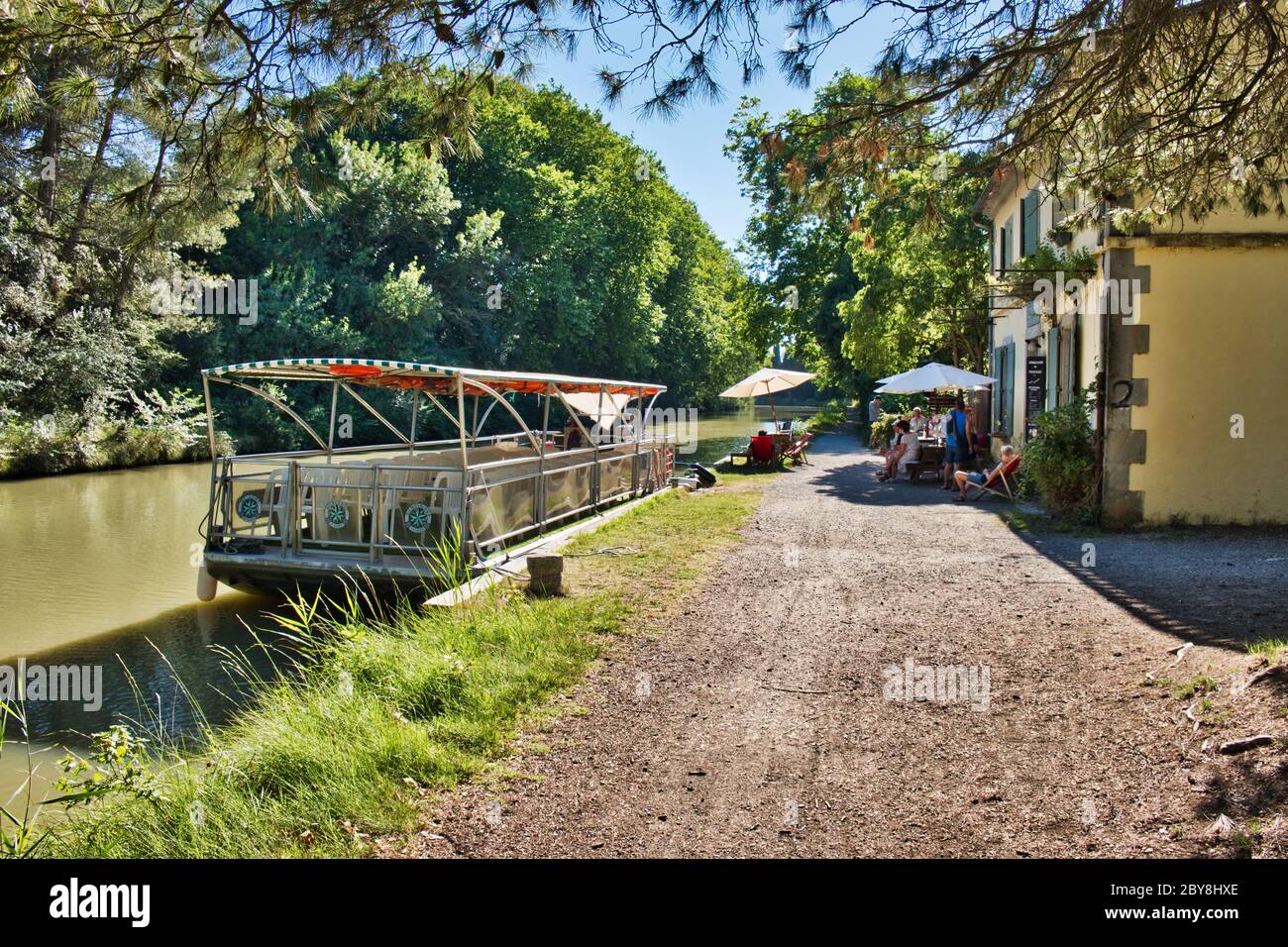 Carcassonne Aude France 07/11/19 Canal du midi chemin de remorquage et chalet de gardiens de écluses. Bateau de visite du canal amarré à côté d'un café. Les vacanciers apprécient un peu de fraîcheur Banque D'Images