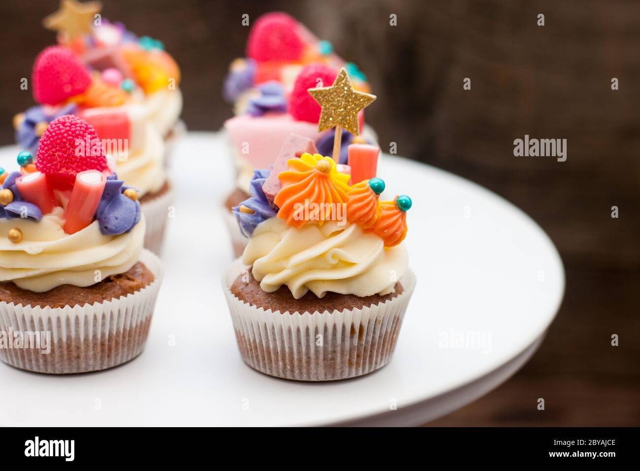 Cupcakes au chocolat avec glaçage au fromage à la crème, marmelade à la pinka et à l'orange, bonbons et topper doré sur fond sombre Banque D'Images