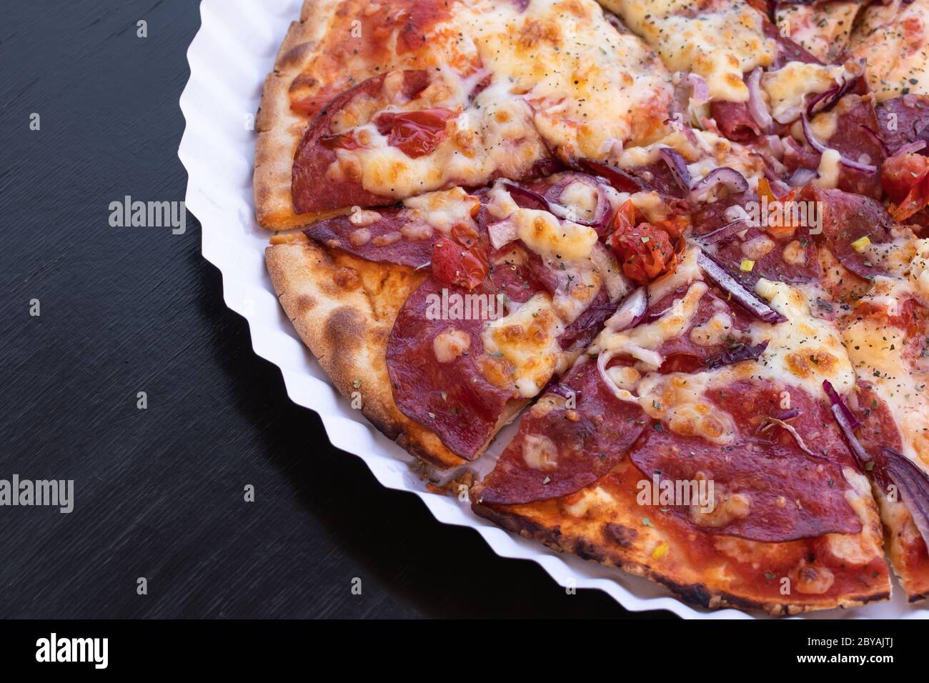 Tranches de pizza avec salami et fromage sur une assiette de papier. Table en bois noir. Copier l'espace. Emplacement vide pour le texte Banque D'Images