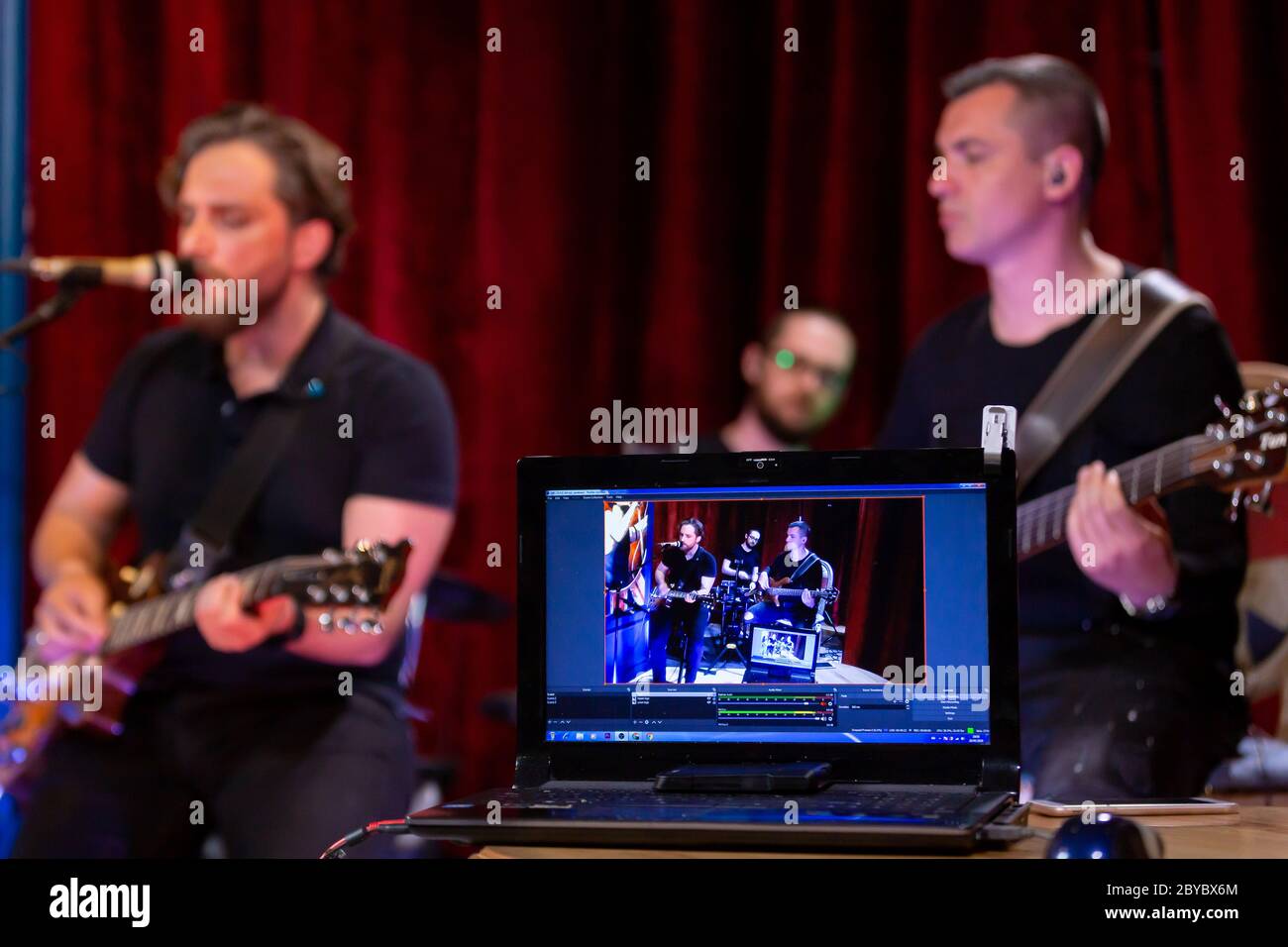 La bande de musiciens jouant de la guitare électrique, de la guitare basse et des tambours pendant le concert diffusé en ligne sur les plateformes de médias sociaux au Bar. Banque D'Images