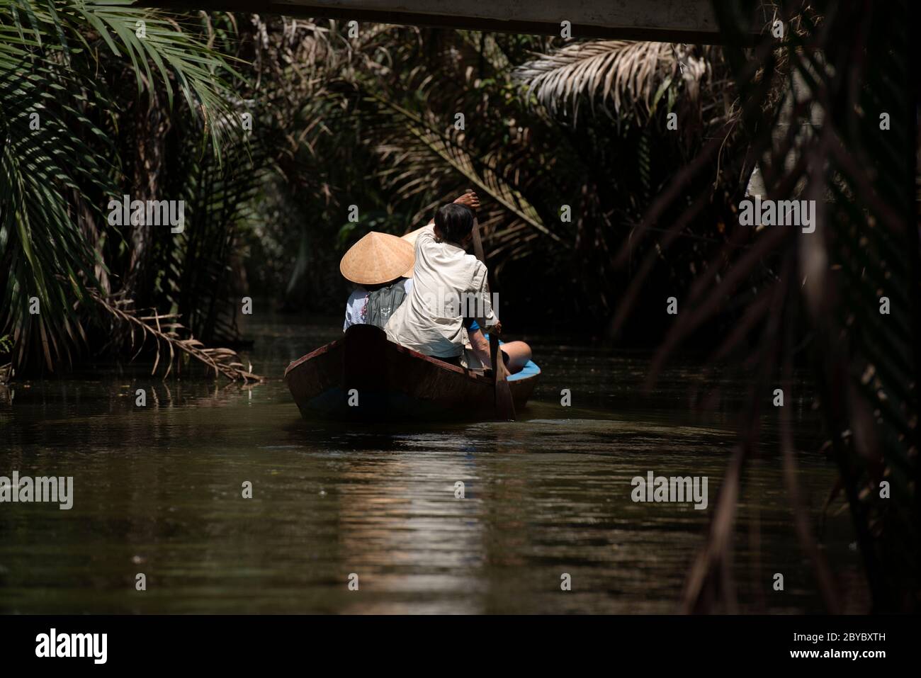 Un guide attire les touristes portant des chapeaux coniques vietnamiens, non la, le long d'une petite rivière à travers une forêt surcultivée dans le delta du Mekon, au sud du Vietnam. Banque D'Images