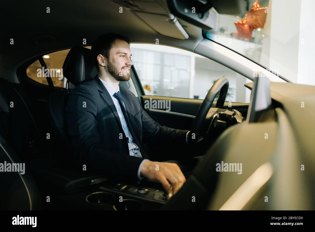 Homme d'affaires à barbe confiant portant une combinaison est assis derrière le volant de la voiture. Banque D'Images