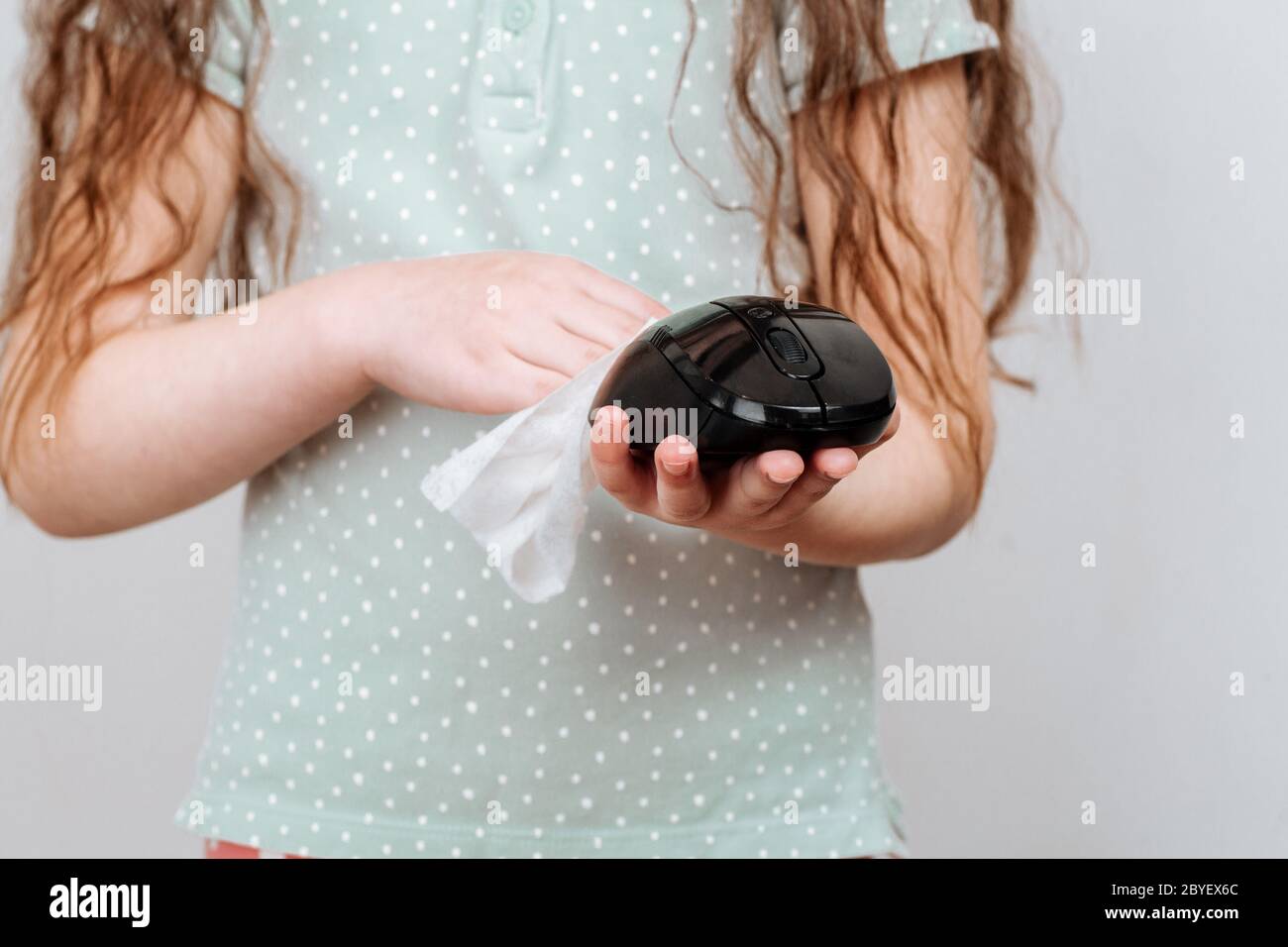 Une fille essuye une souris d'ordinateur avec un chiffon désinfectant. Combattre les virus et les bactéries pendant une pandémie Banque D'Images
