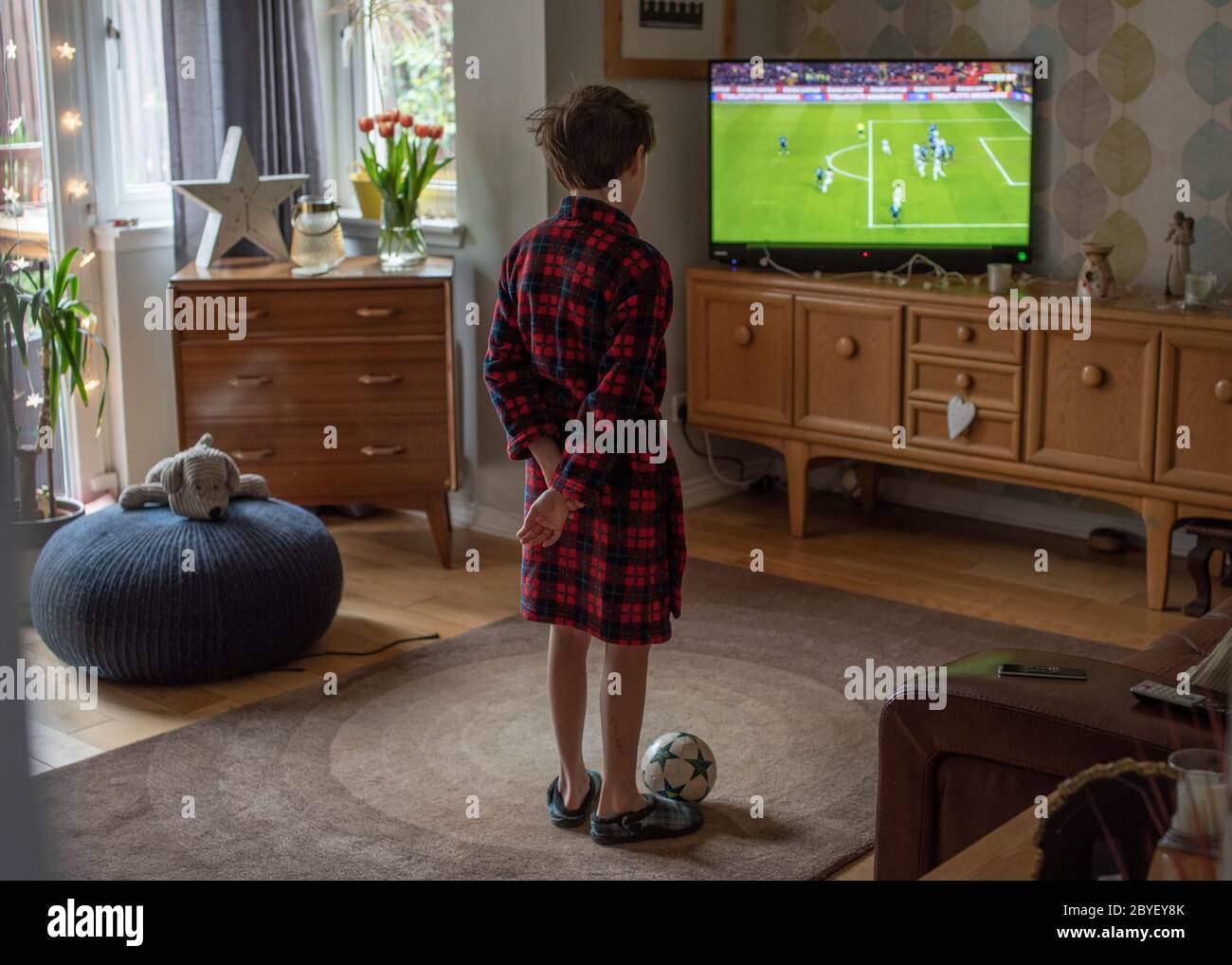Covid 19, l'éducation à domicile image D'un enfant à la maison dans une robe de chambre et des pantoufles, regardant s'ennuyer de la scolarisation à la maison et de trouver difficile d'obtenir la mo Banque D'Images