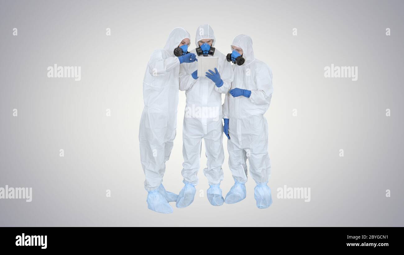 Médecins ou scientifiques portant des combinaisons de matières dangereuses travaillant ensemble sur une tablette numérique sur fond dégradé. Banque D'Images
