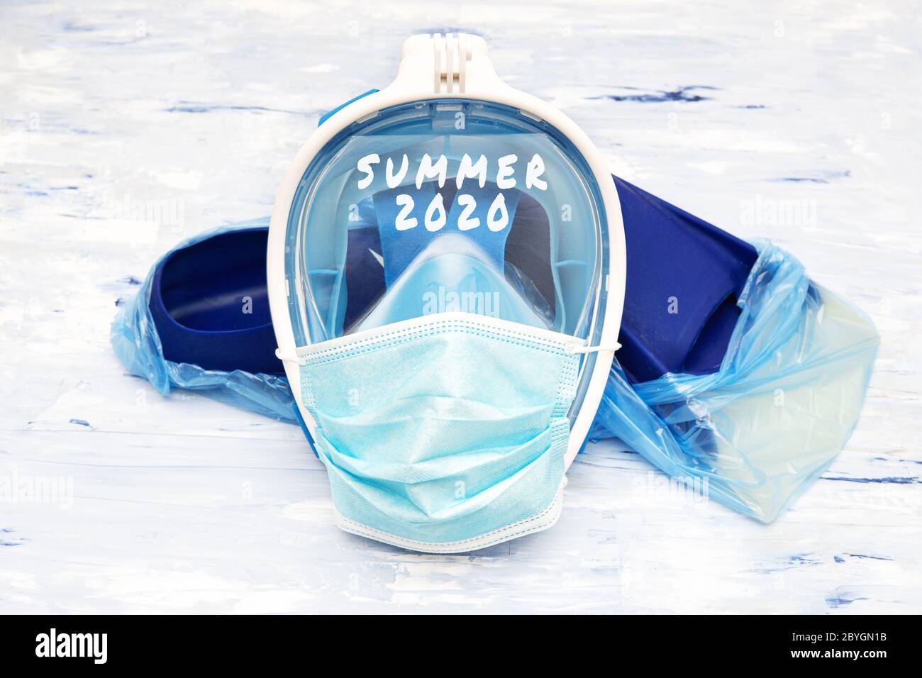 Texte ÉTÉ 2020 écrit sur un masque de plongée complet couvert d'un masque chirurgical jetable couché sur des ailettes bleues dans des surchaussures de protection. Annuler Banque D'Images