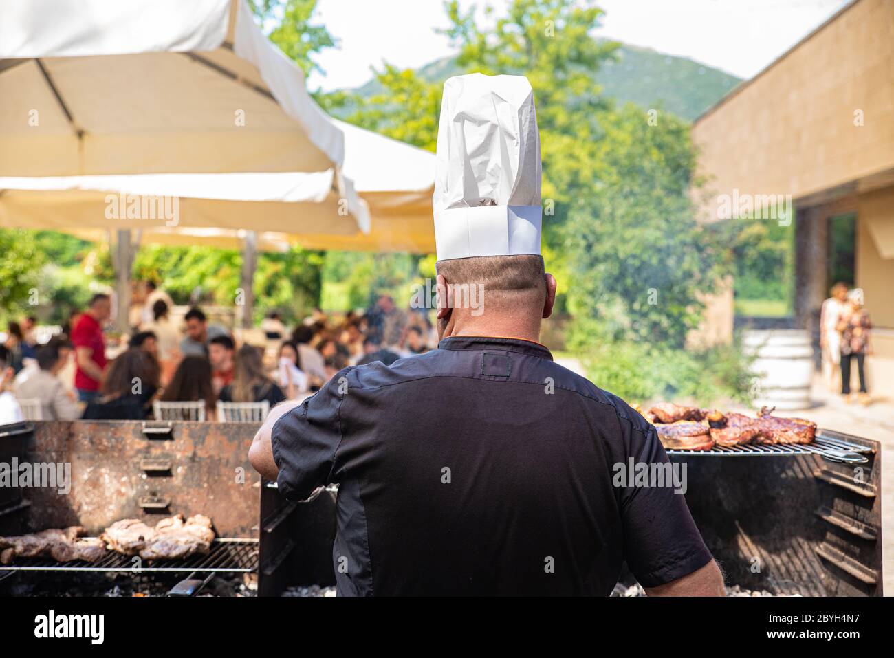 Italie. Chef de cuisine avec chapeau de chef pris de derrière tout en  cuisant la viande dans le barbecue. Restaurant extérieur Photo Stock - Alamy