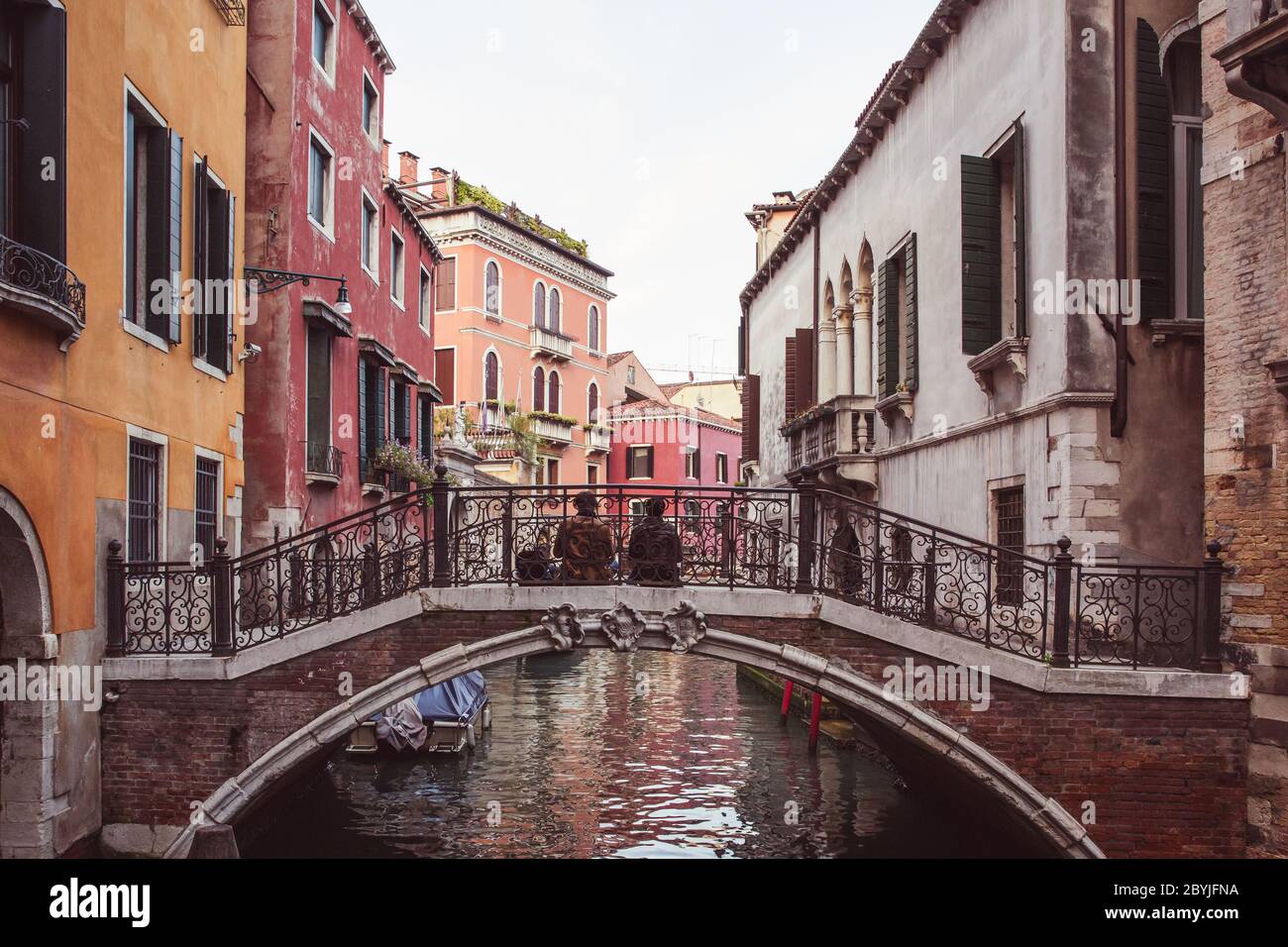 Deux amoureux assis côte à côte sur un pont au-dessus d'un canal parmi des bâtiments roses à Venise, Italie Banque D'Images