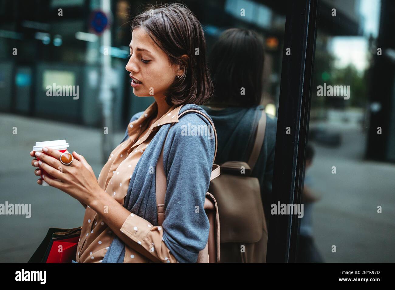 Une jeune femme heureuse à boire du café et à marcher avec des sacs après avoir fait du shopping en ville. Banque D'Images