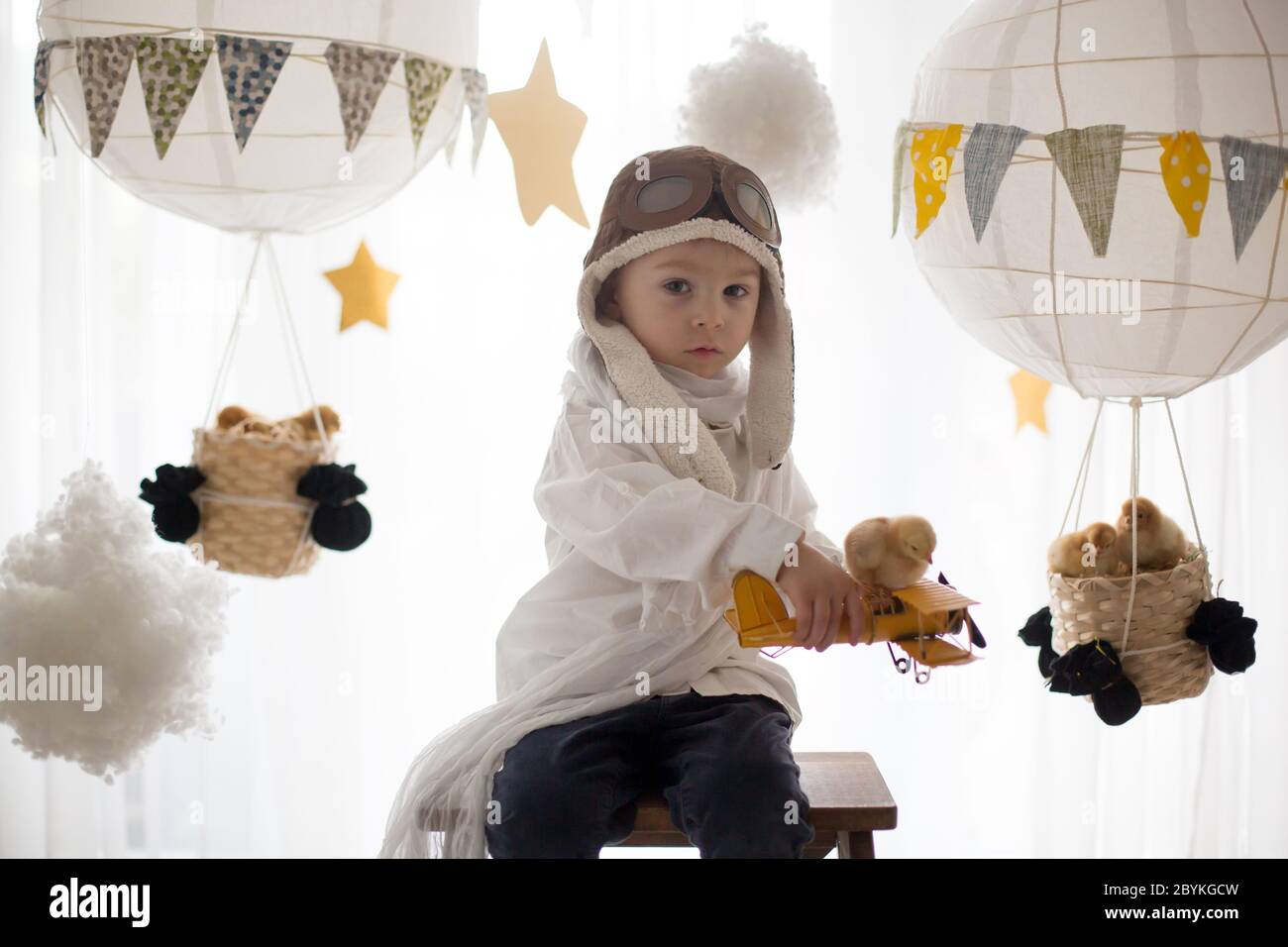 Mignon petit enfant, garçon, jouant avec des poussins à la maison, prétendant qu'il vole dans le ciel, pilote avec avion et poussin d'animal de compagnie Banque D'Images