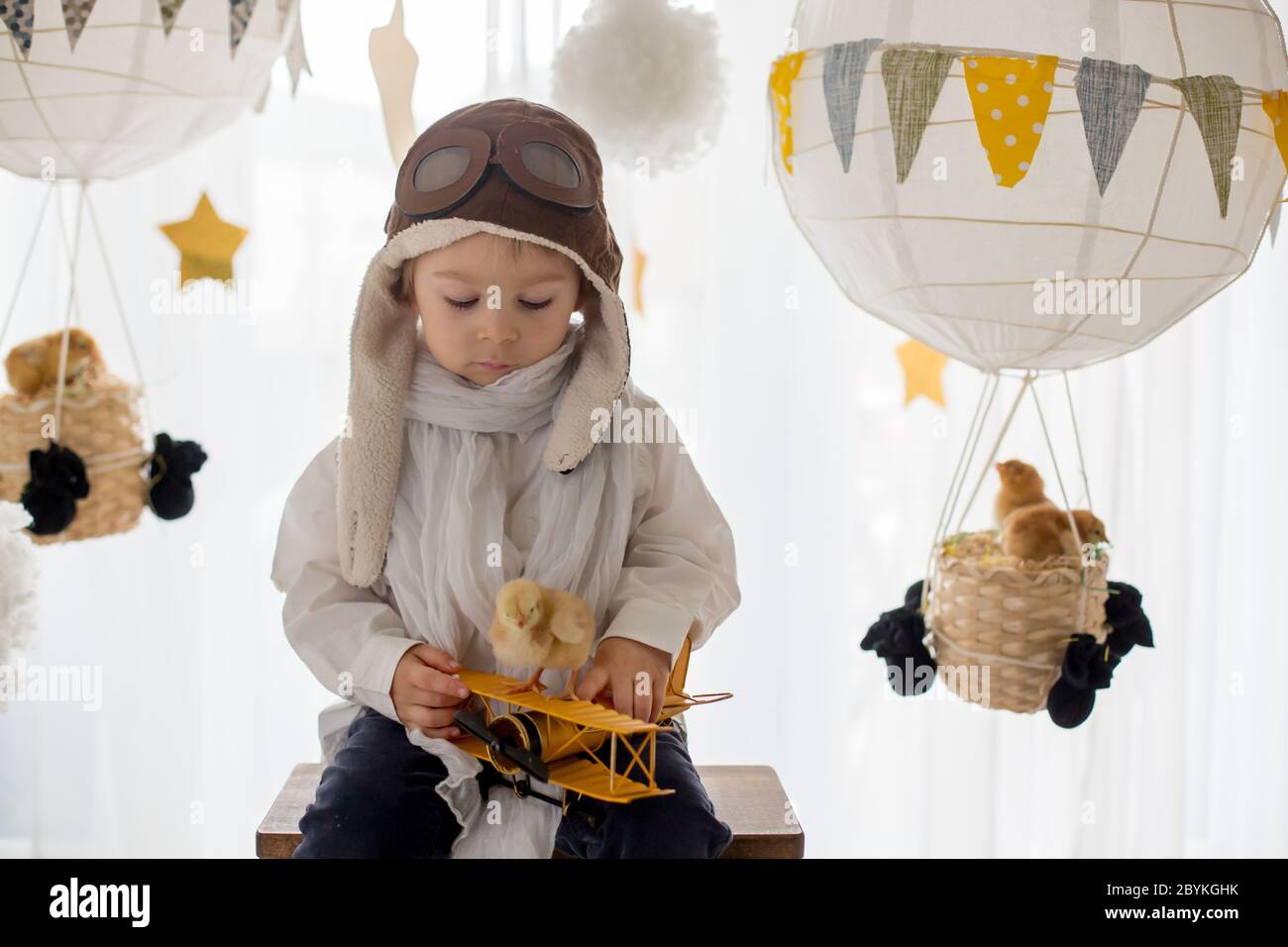 Mignon petit enfant, garçon, jouant avec des poussins à la maison, prétendant qu'il vole dans le ciel, pilote avec avion et poussin d'animal de compagnie Banque D'Images