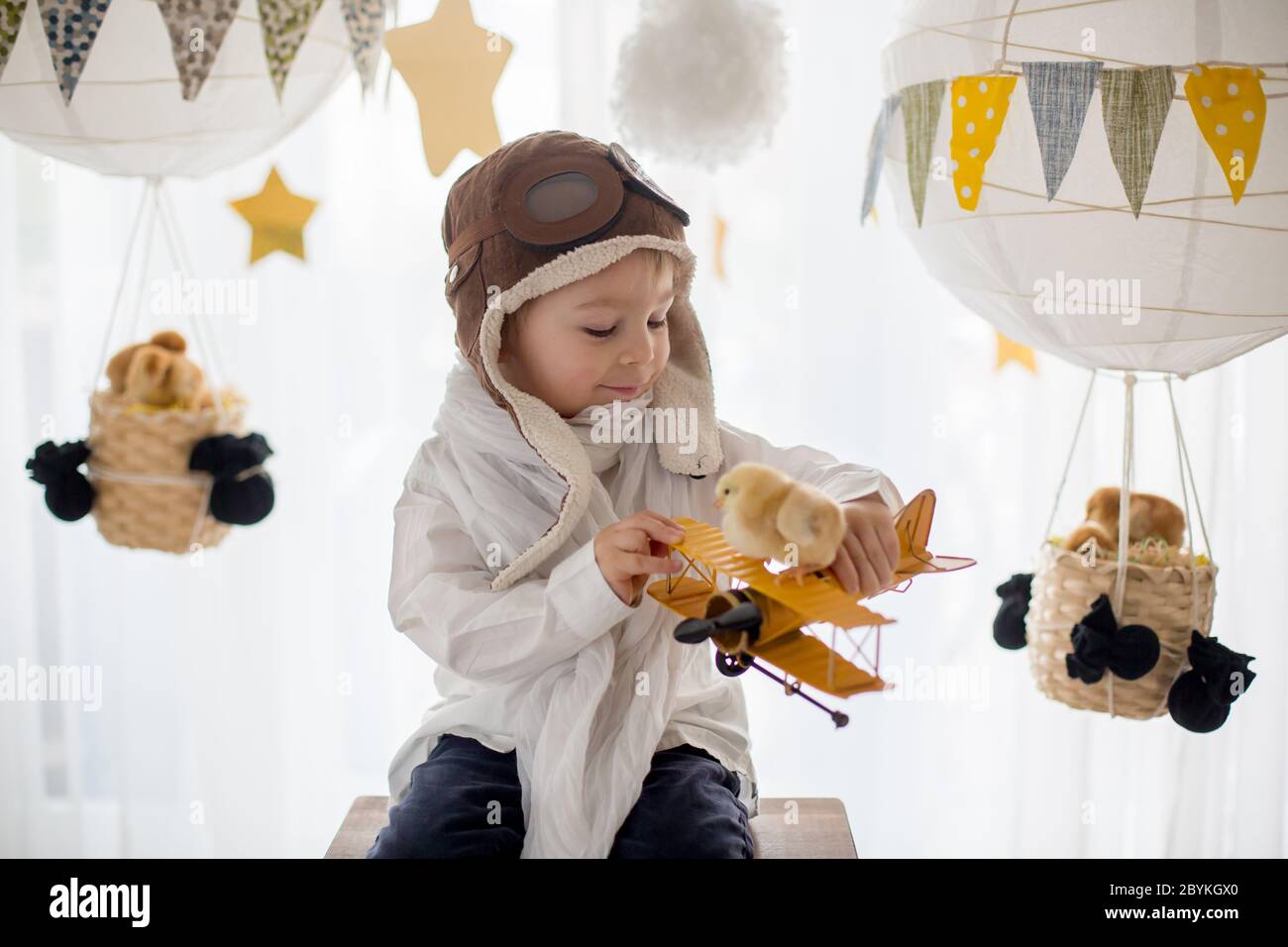 Mignon petit enfant, garçon, jouant avec des poussins à la maison, prétendant qu'il vole dans le ciel, pilote avec avion et poussin d'animal de compagnie Banque D'Images