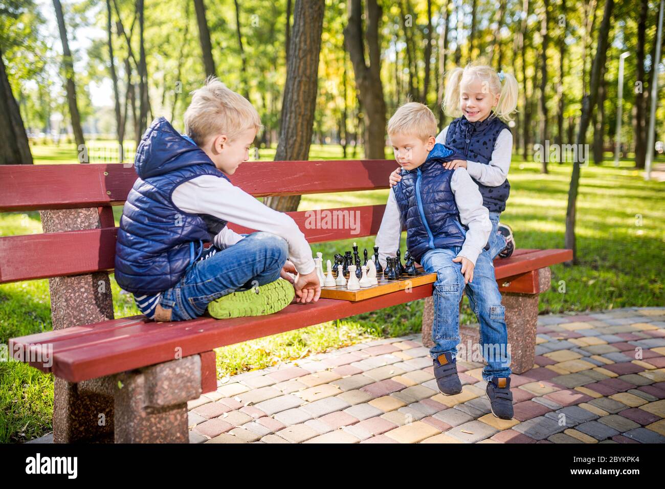 Petits écoliers jouant aux échecs dans le parc sur le banc. Vacances d'été, jeux intellectuels. Club d'échecs pour enfants. Bonne enfance et enfants Banque D'Images