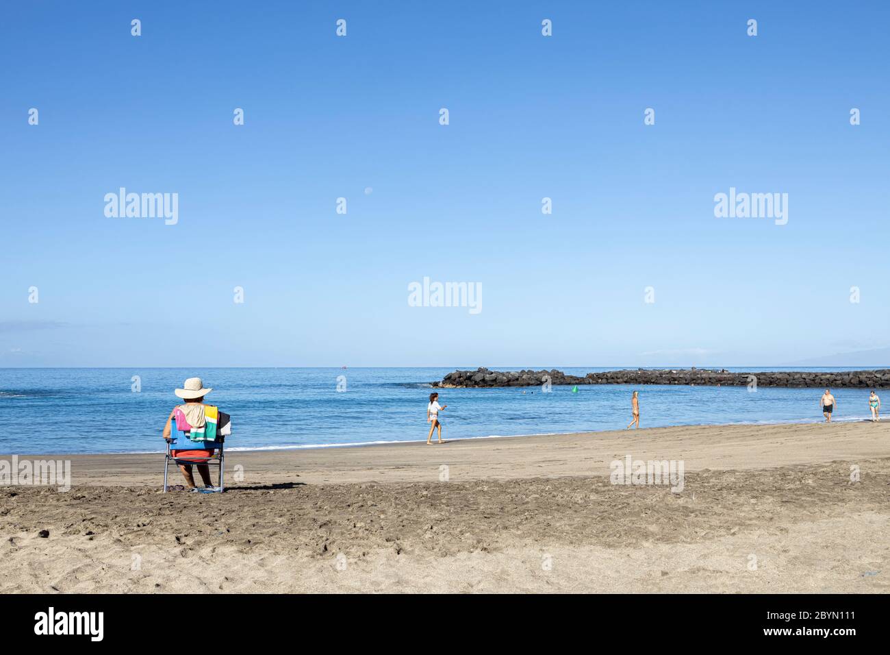 Femme en chapeau de paille assise sur une chaise portable sur la plage Playa del Duque, Costa Adeje, Tenerife, Iles Canaries, Espagne Banque D'Images