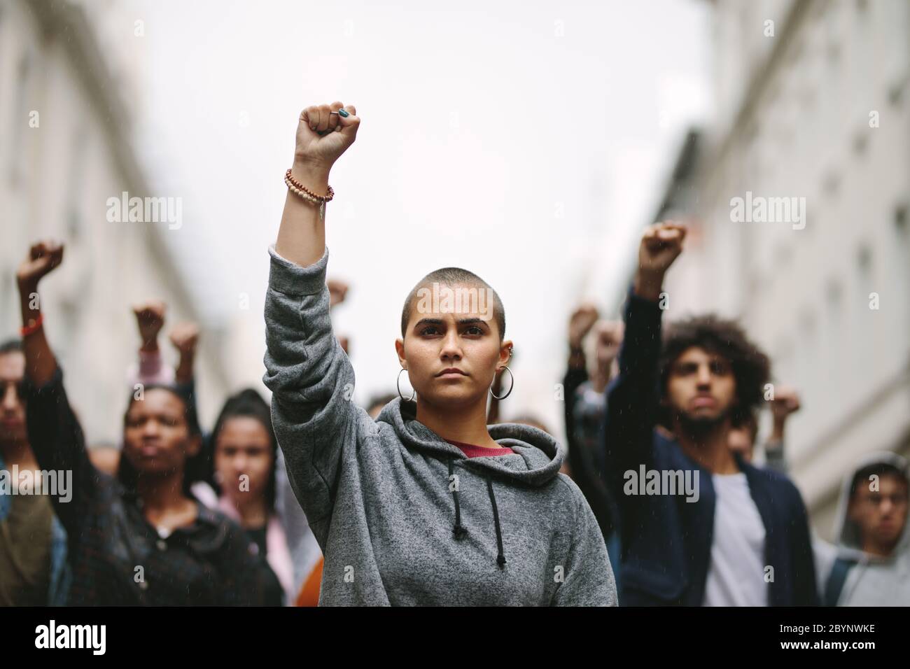 Groupe de jeunes manifestant contre le gouvernement sur la route avec leurs poings levés. Des personnes multiethniques protestant dans la rue. Banque D'Images