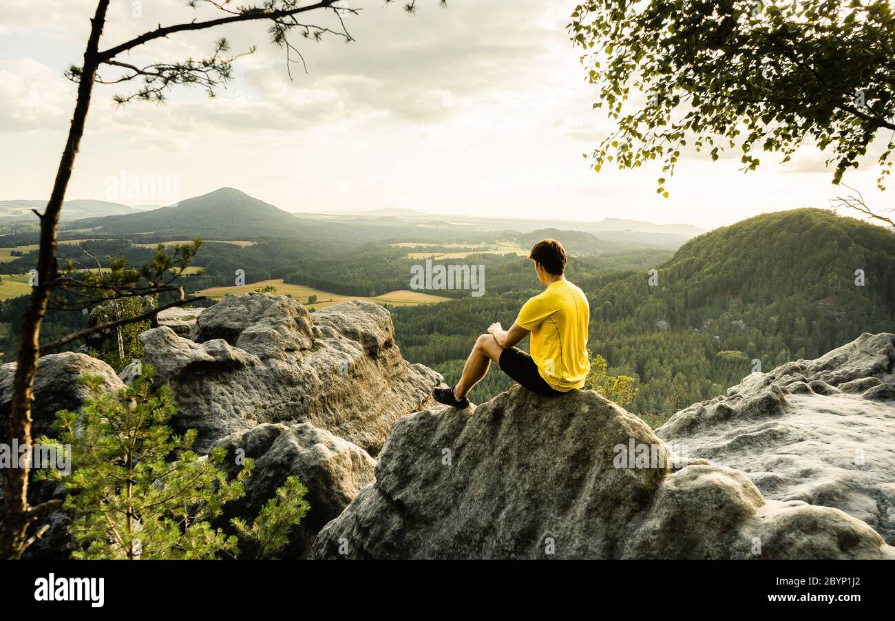 Randonneur assis sur les rochers, regardant loin et apprécier la nature. Vêtements de sport confortables. Vue depuis le mur de Vilemin jusqu'à Mary's. République tchèque Banque D'Images