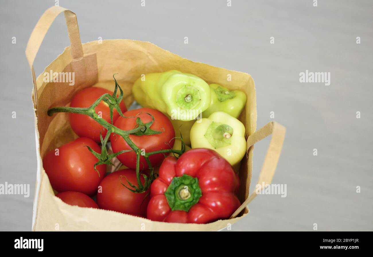 Vue de dessus du sac de papier d'épicerie rempli de tomates et de poivrons verts sur fond gris. Sac de papier complet avec légumes. Banque D'Images